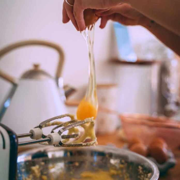 Hands breaking an egg into cake mix with a mixer on the side, all for a writing exercise.