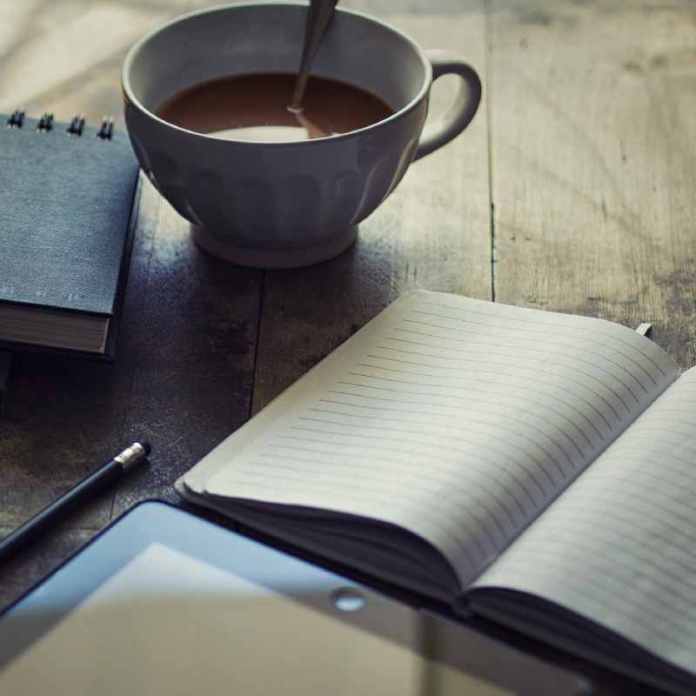 A notebook, tablet and coffee on a wooden table, Gail Owen's favourite writing tools.