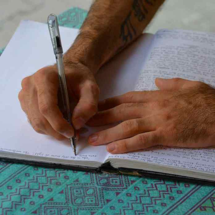 A student's hand scribbling inspired notes in  notebook against a turquoise table cloth in a Cornish creative writing class.