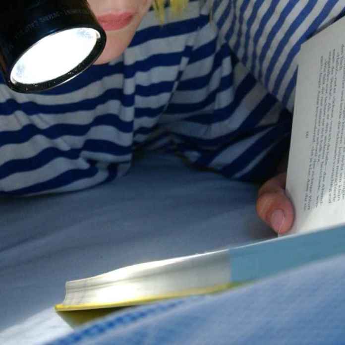 A child in a striped pyjama top under a striped duvet, reading their book with a torch. This is something that I, Gail Owen, did a lot as a child. I loved stories and reading so much that after my mum had told me it was time to go to sleep, I would pull my duvet up over my head and keep reading my book with a torch.
